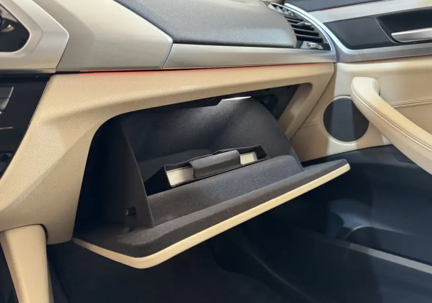 Intérieur beige du BMW X3 xDrive30d 2018, vue côté passager sur la boîte à gants ouverte avec manuel visible.