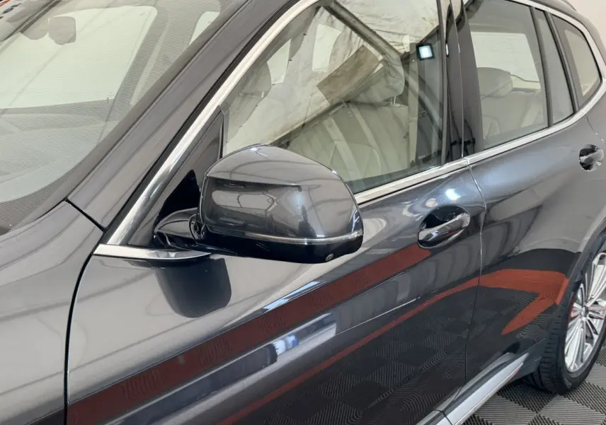 Gros plan sur le côté gauche gris foncé d’un BMW X3 2018, mettant en valeur la poignée et le rétroviseur.
