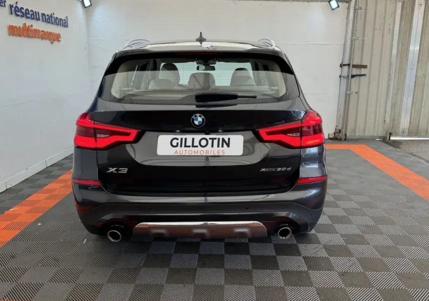 Vue arrière d'un BMW X3 xDrive30d gris foncé avec feux LED allumés et double sortie d'échappement visible.