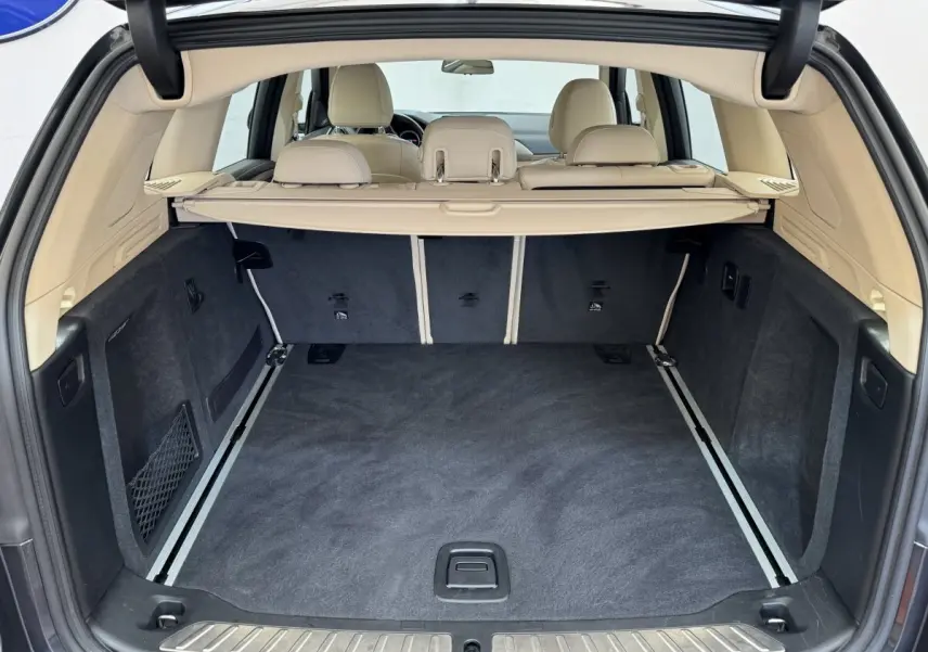 Coffre ouvert d'un BMW X3 gris foncé, vue arrière montrant l'intérieur beige et le tapis noir du coffre spacieux.