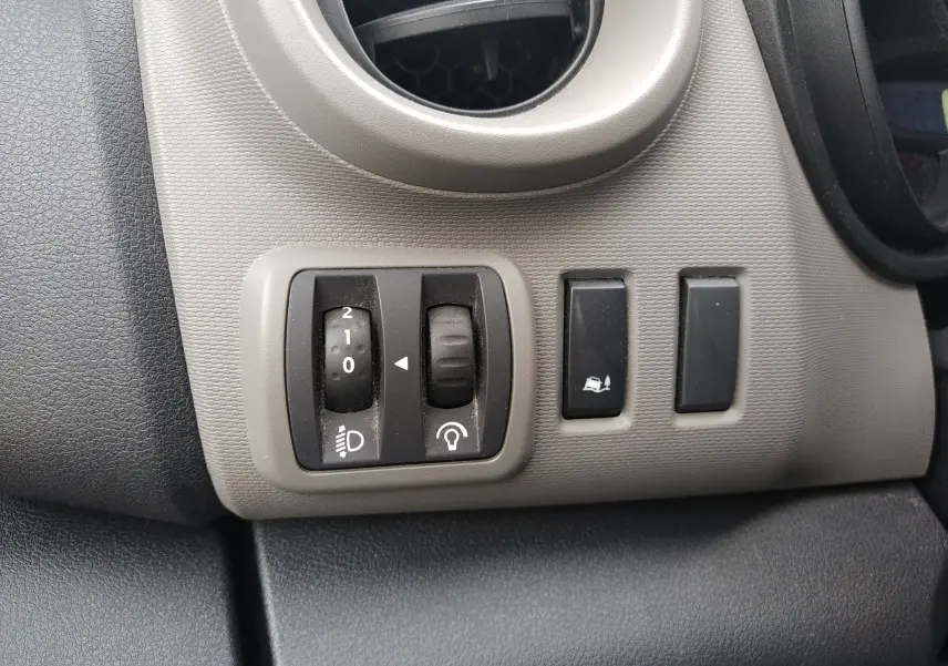 Gros plan sur les commandes d'éclairage et d'assistance au freinage du tableau de bord gris du Renault Trafic Microbus blanc 2016.