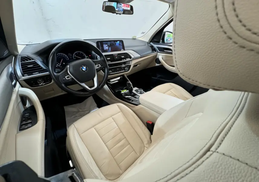 Intérieur beige clair du BMW X3 2018 vu côté conducteur, avec tableau de bord et écran tactile central visibles.