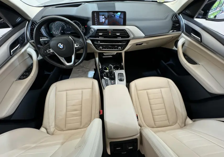Intérieur clair du BMW X3 2018 vu de face, avec tableau de bord moderne et écran tactile central affichant la caméra de recul.