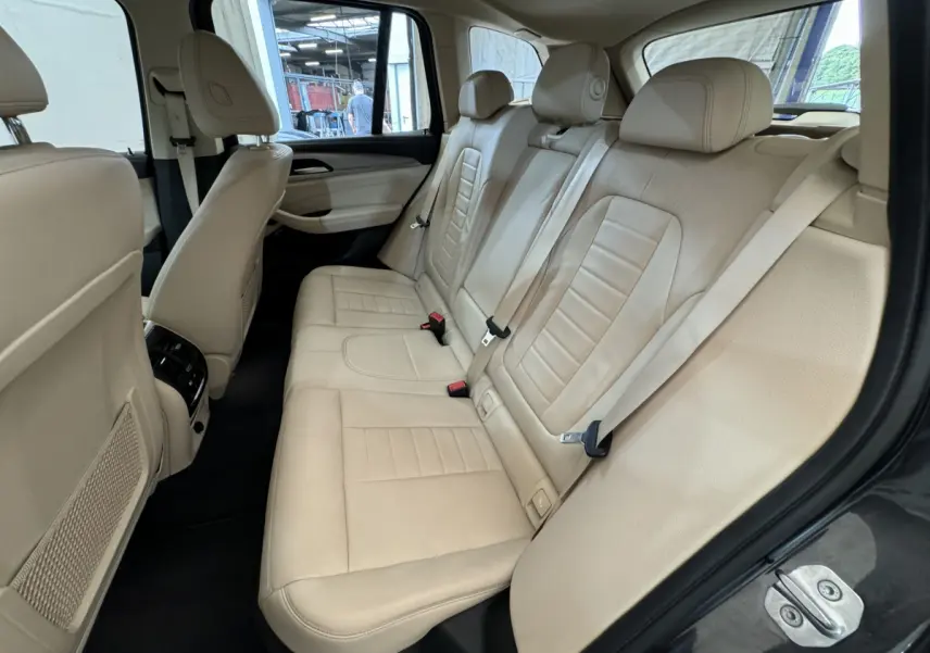 Vue intérieure côté droit des sièges arrière en cuir beige du BMW X3 xDrive30d 2018 avec appuie-têtes et ceintures visibles.