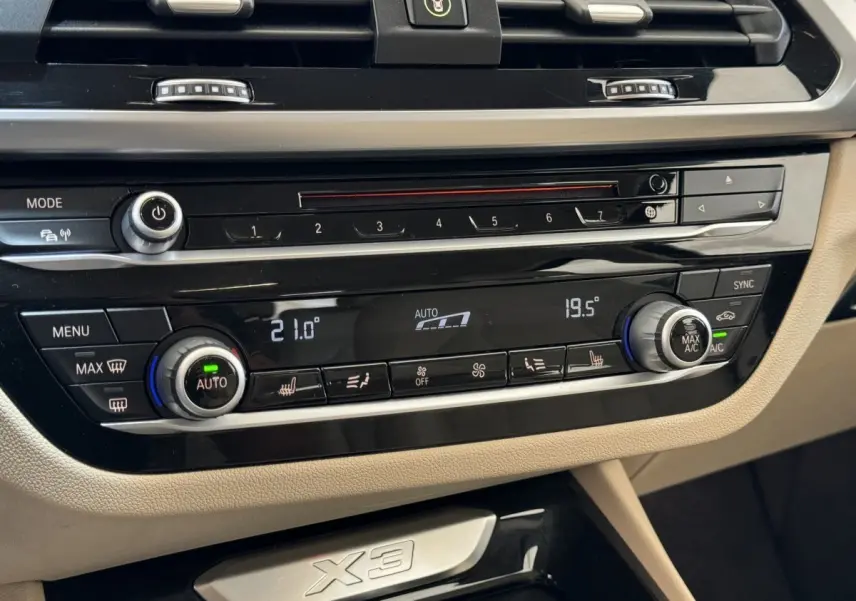 Détail du tableau de bord beige du BMW X3 2018 avec commandes climatisation digitale et finition brillante noire.