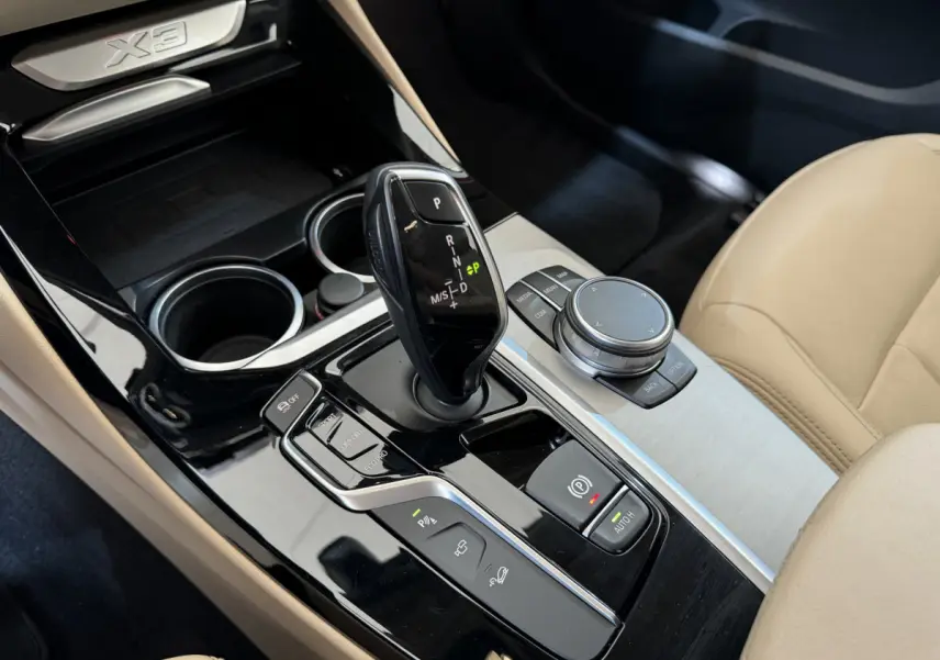 Gros plan sur la console centrale noire et argentée du BMW X3 2018 avec levier de vitesse et siège beige visible côté droit.
