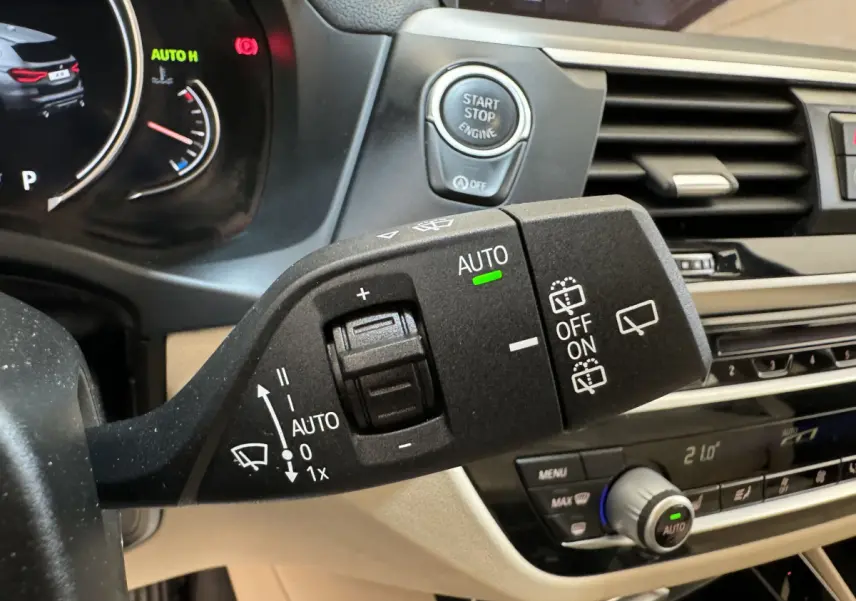 Gros plan sur la commande d’essuie-glace et le bouton start-stop du tableau de bord beige d’un BMW X3 gris foncé 2018.