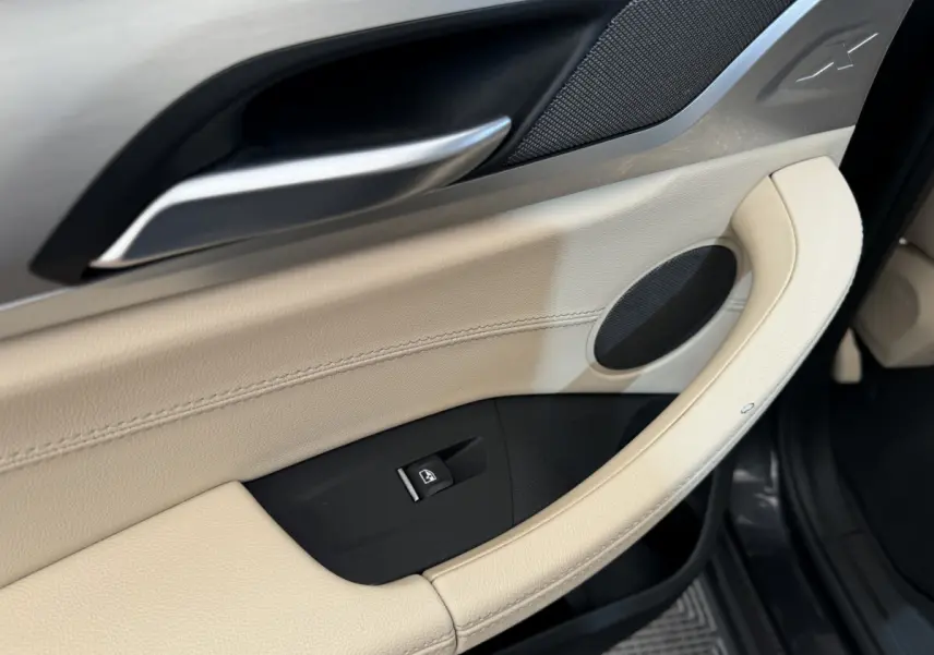 Gros plan sur la garniture beige et noire de la porte côté conducteur du BMW X3 gris foncé 2018 avec poignée alu.
