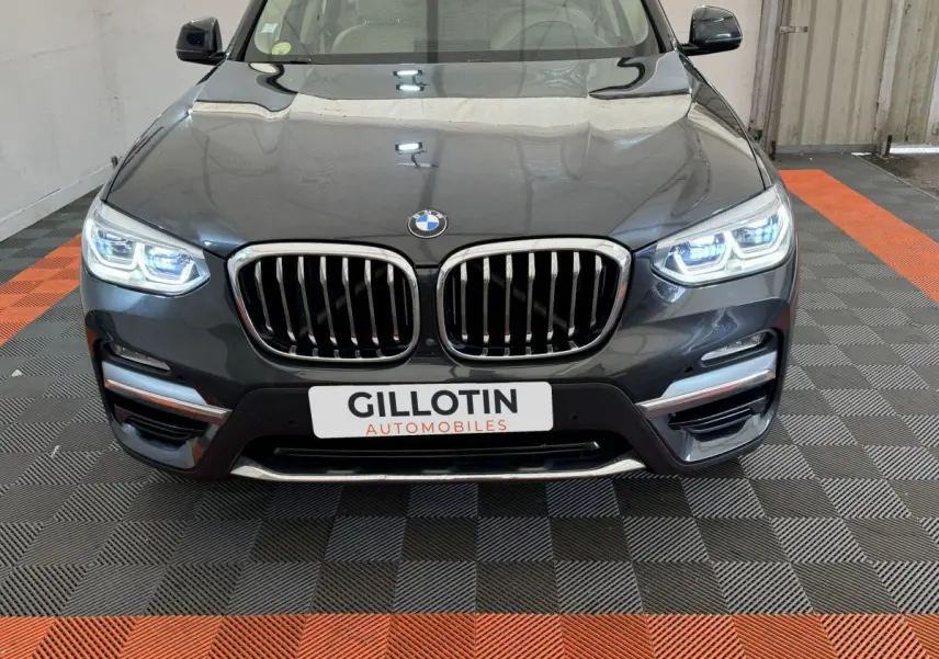 Vue frontale rapprochée d’un BMW X3 gris foncé avec phares LED allumés et calandre double haricot distinctive.