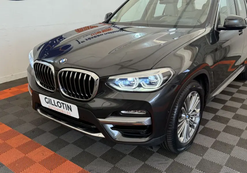 Vue 3/4 avant droit d'un BMW X3 gris foncé avec calandre chromée et phares LED allumés dans un showroom.