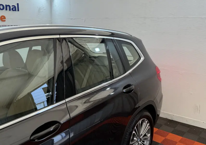 Vue côté arrière droit d'un BMW X3 gris foncé avec jantes alliage et intérieur clair visible à travers les vitres.