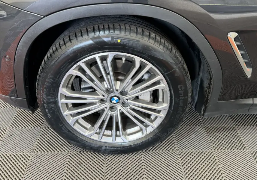 Gros plan sur la roue avant gauche d'un BMW X3 gris foncé avec jante alliage multi-branches et logo BMW central.