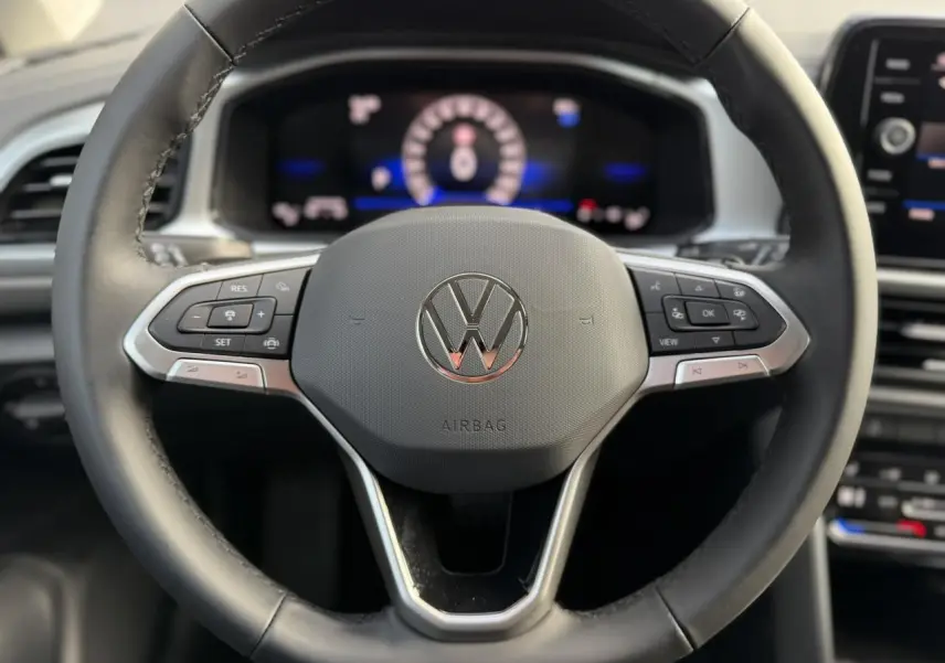 Gros plan sur le volant en cuir multifonction noir du Volkswagen T-Roc 1.5 TSI 150 DSG Life 30 Years, tableau de bord digital en arrière-plan flou.