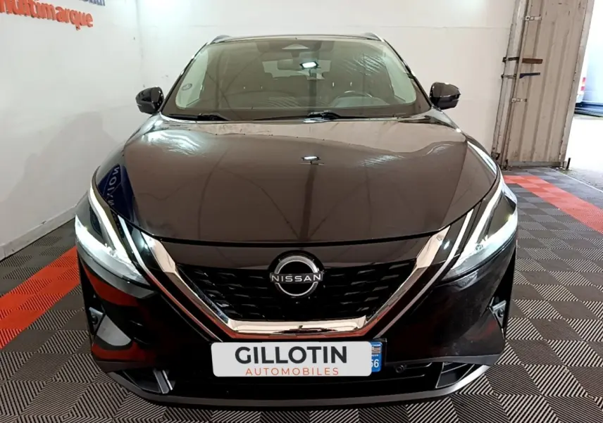 Vue avant d’un Nissan Qashqai e-Power noir, avec calandre chromée et phares LED allumés dans un showroom.