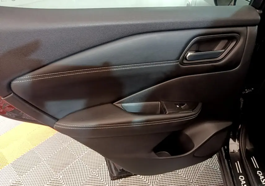 Vue intérieure côté gauche de la porte avant noire du Nissan Qashqai e-Power avec surpiqûres blanches et poignée alu.
