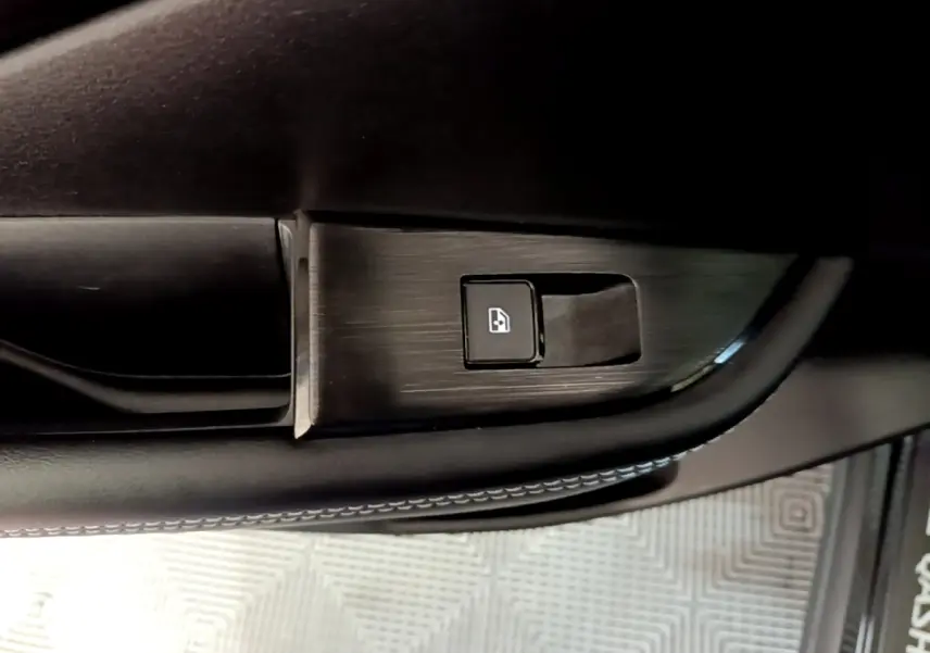 Gros plan sur le bouton de commande de lève-vitre côté conducteur du Nissan Qashqai e-Power noir, intérieur cuir et finition aluminium.