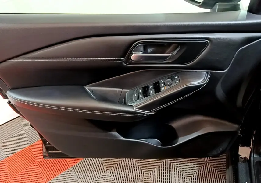 Vue intérieure côté gauche de la porte noire du Nissan Qashqai e-Power avec commandes des vitres et poignée alu.