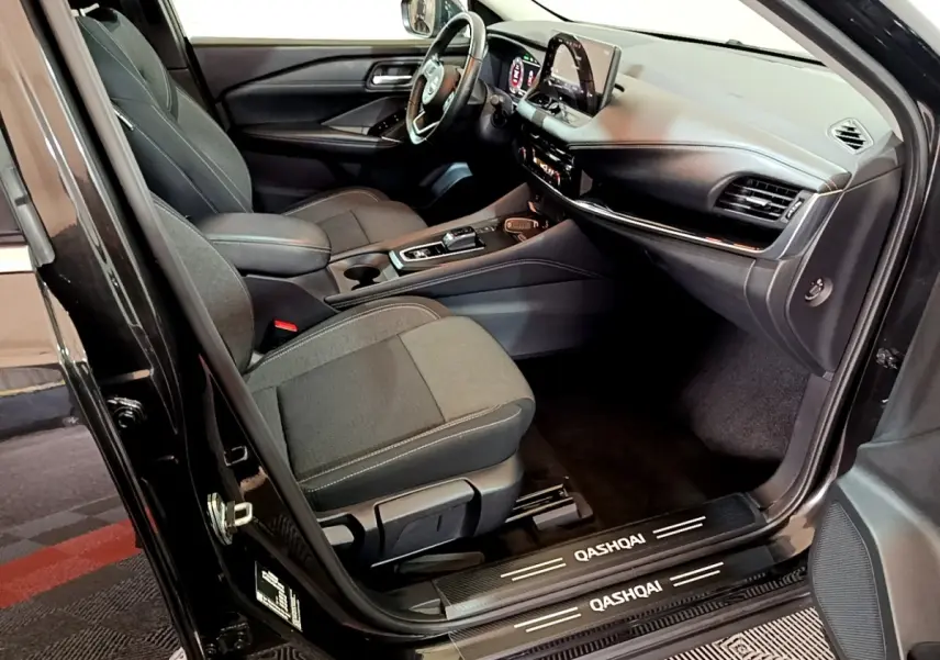 Intérieur avant droit du Nissan Qashqai e-Power noir 2023, volant cuir alu et écran tactile 12,3 pouces visible.