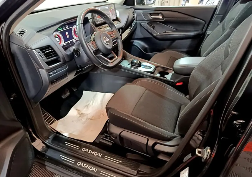 Intérieur avant droit du Nissan Qashqai noir 2023, volant cuir alu, tableau de bord digital et sièges tissu gris.