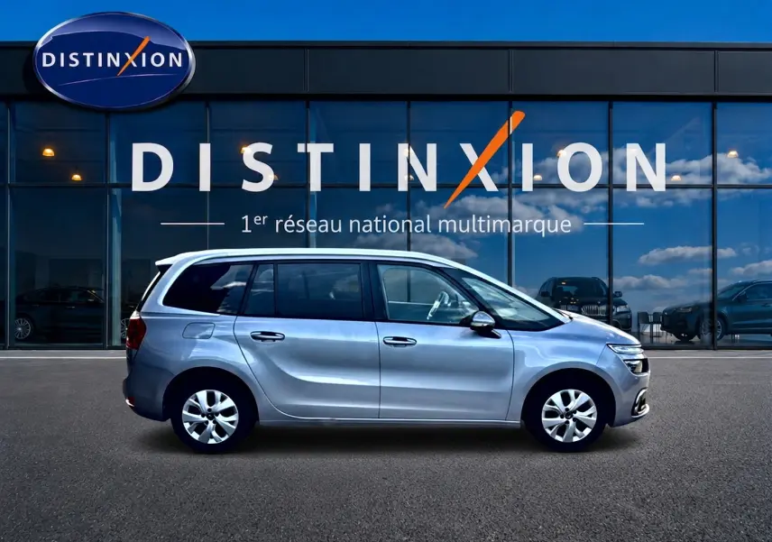 Profil côté gauche d'un Citroën Grand C4 Spacetourer gris alu 2021 garé devant une vitrine avec logo Distinxion.