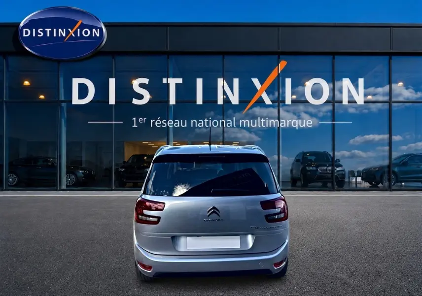 Vue arrière d'un Citroën Grand C4 Spacetourer gris alu garé devant une vitrine avec logo Distinxion.