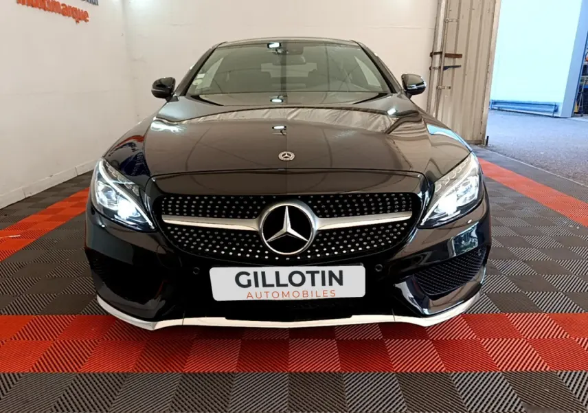 Vue frontale d'une Mercedes Classe C Coupé noire avec calandre diamantée et phares LED allumés dans un showroom.