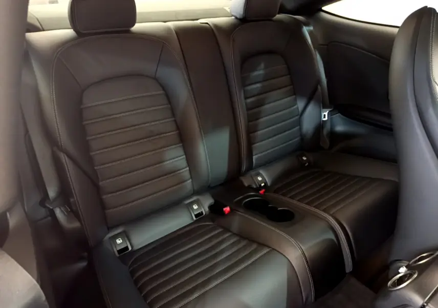 Vue intérieure sur la banquette arrière en cuir noir du Mercedes Classe C Coupé C 220 d Fascination 2018, avec accoudoir central et porte-gobelets.