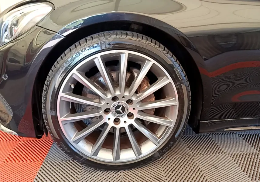 Gros plan sur la roue avant gauche d'une Mercedes Classe C Coupé noire, jante alliage multibranches et logo central visible.