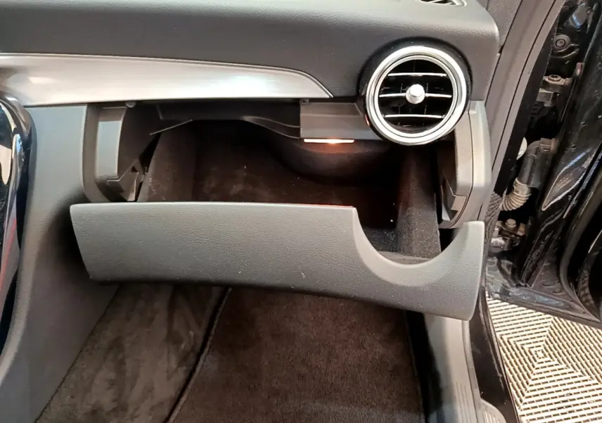 Gros plan sur la boîte à gants ouverte côté passager d'une Mercedes Classe C Coupé noire, intérieur sombre et aérateurs ronds visibles.