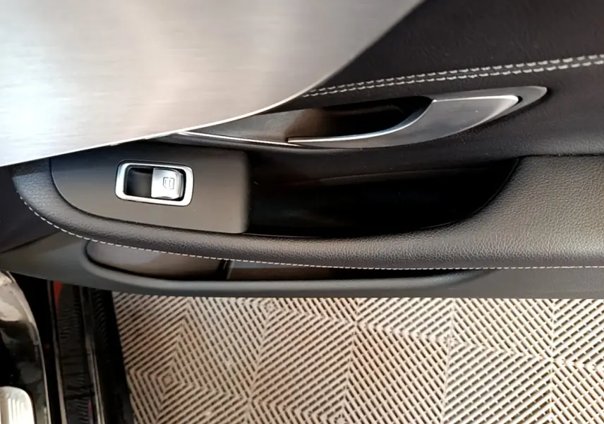 Poignée intérieure côté gauche avec bouton de verrouillage sur porte en cuir noir et insert aluminium d'une Mercedes Classe C Coupé noire.