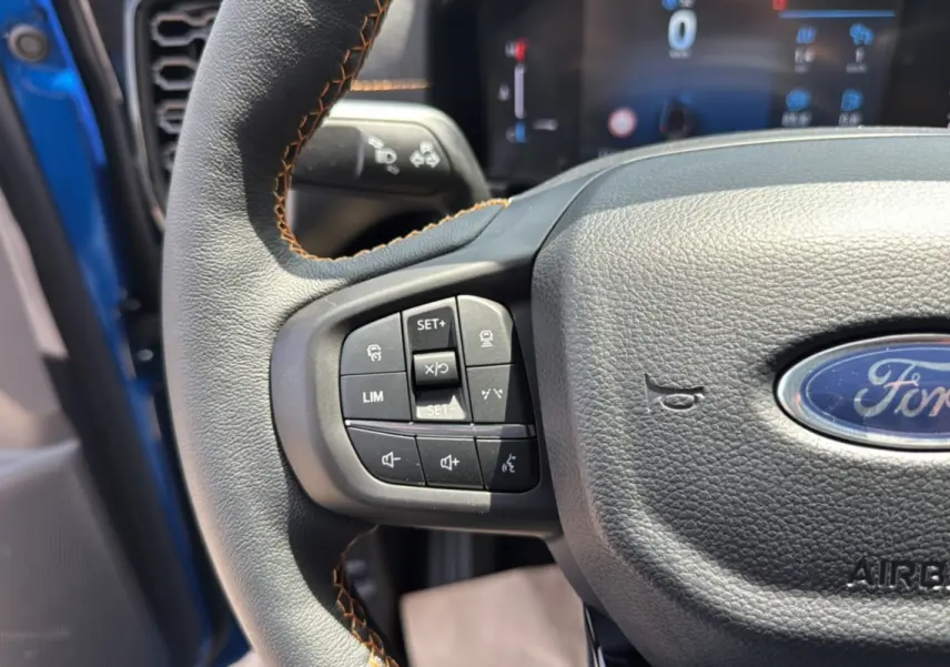 Gros plan sur le volant cuir multifonctions du Ford Ranger Bleu Lightning, avec commandes intégrées et tableau de bord flou en arrière-plan.