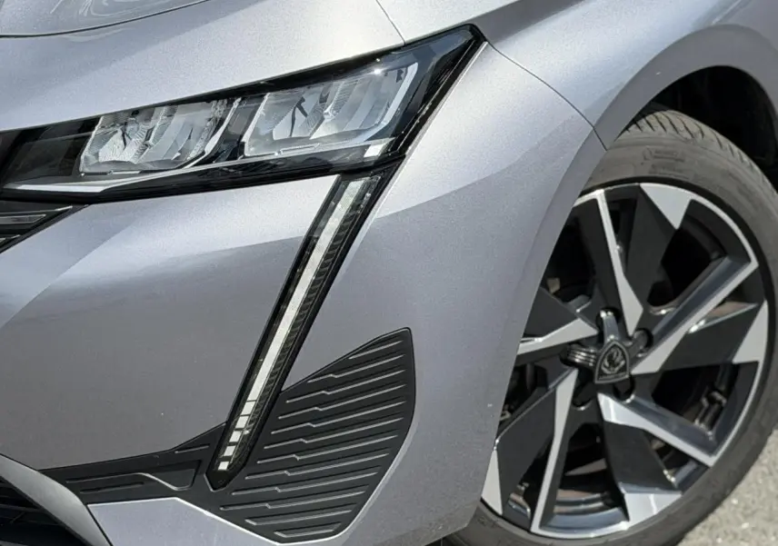 Gros plan sur le phare avant droit et la jante alliage 17'' gris Artense métallisée du Peugeot 308 2025.