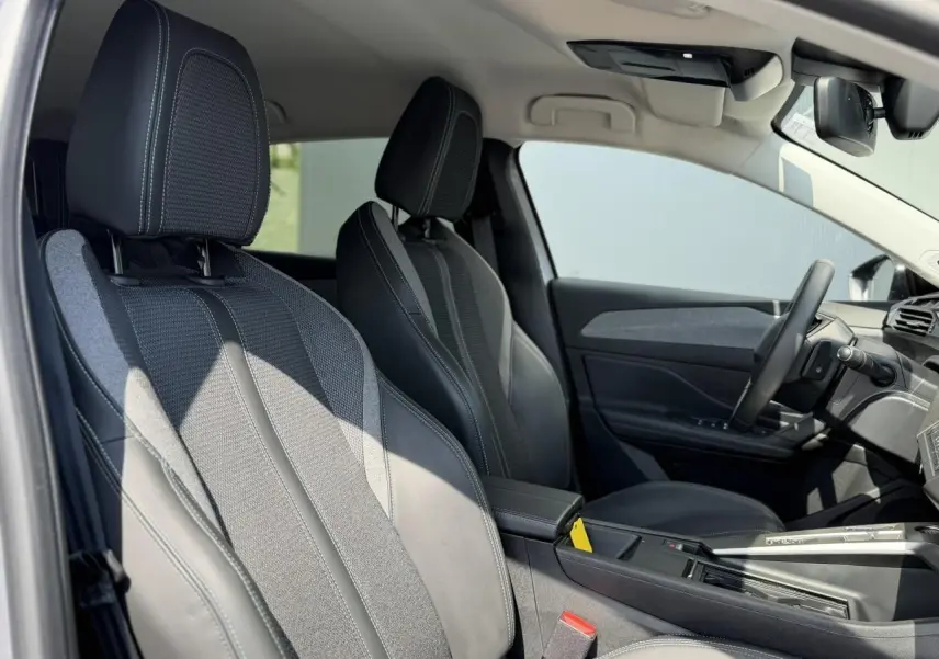 Vue intérieure côté conducteur de la Peugeot 308 2025 avec sièges en cuir et tissu gris, volant cuir et accoudoir central.
