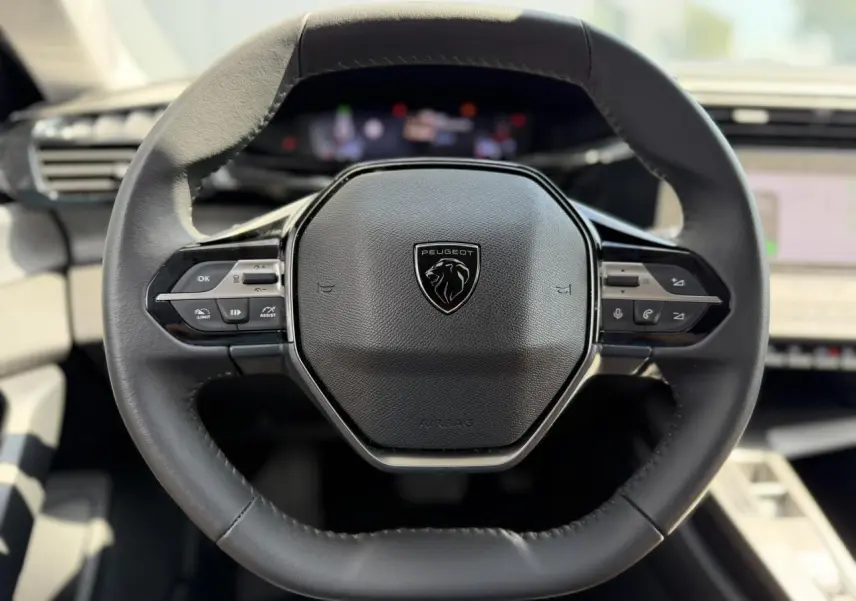 Vue rapprochée du volant cuir noir de la Peugeot 308 2025 avec commandes intégrées et logo central lion.