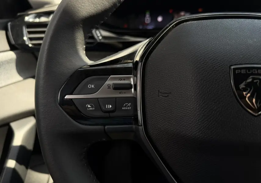 Gros plan sur le volant cuir noir de la Peugeot 308 2025, avec commandes intégrées et logo lion central.