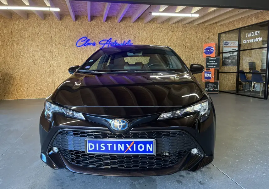 Vue frontale d'une Toyota Corolla 1.8 122 Dynamic noire avec calandre large et phares LED fins dans un showroom.