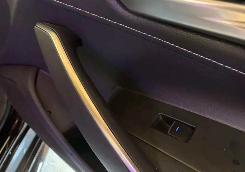 Gros plan sur la poignée intérieure et le bouton de lève-vitre côté gauche d'une Toyota Corolla noire, finition tissu.