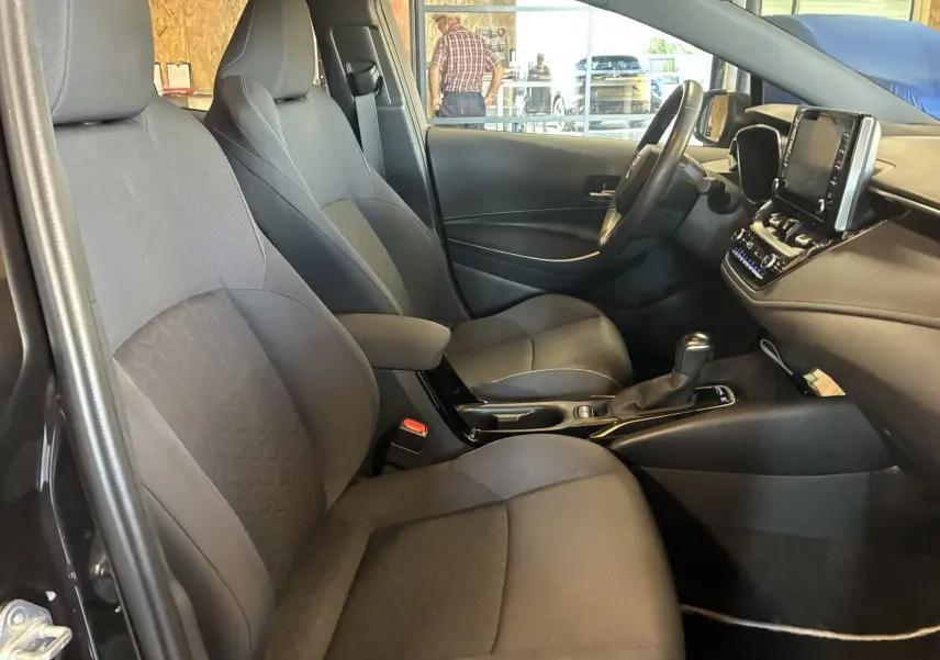 Vue intérieure côté conducteur de la Toyota Corolla 1.8 122 Dynamic 2020 avec sièges tissu noirs et tableau de bord moderne.