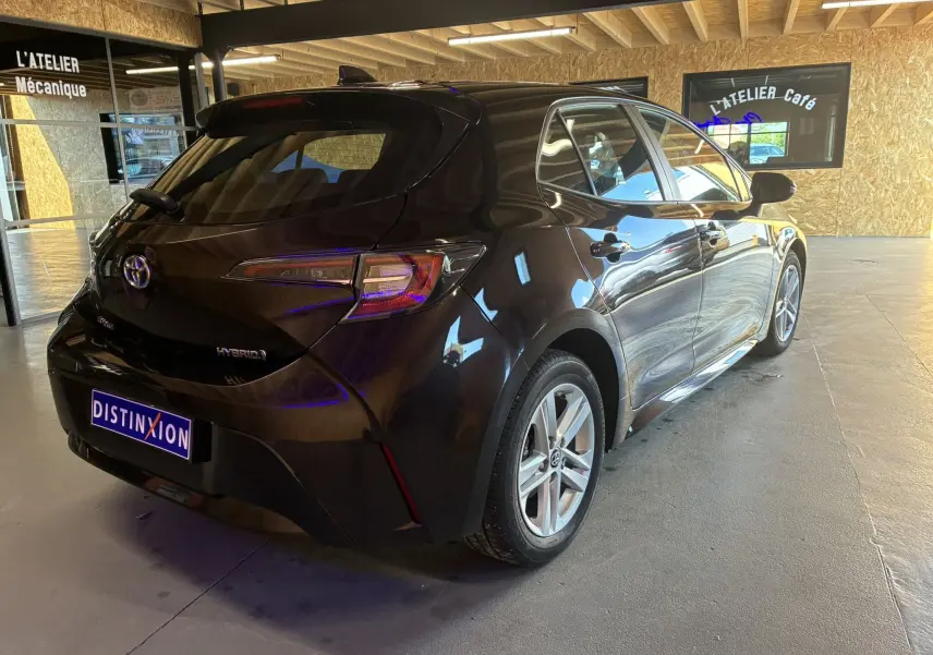 Vue 3/4 arrière droite d'une Toyota Corolla noire hybride 2020 avec jantes alu, stationnée en intérieur lumineux.