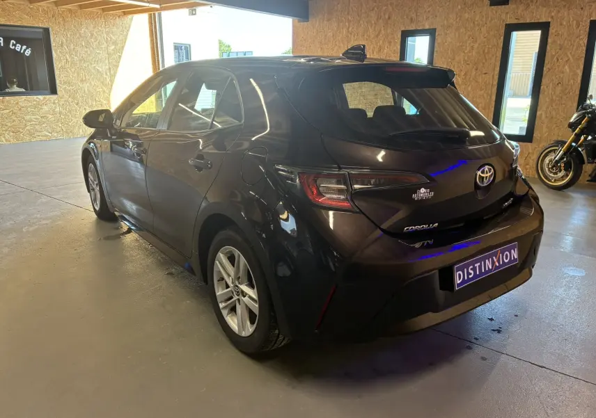 Toyota Corolla 1.8 122 Dynamic noire vue 3/4 arrière droit en intérieur avec jantes alu et feux LED distinctifs.