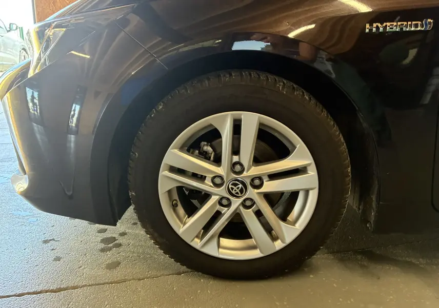 Gros plan sur la roue avant gauche de la Toyota Corolla noire 1.8 122 Dynamic avec jante alu et badge Hybrid visible.