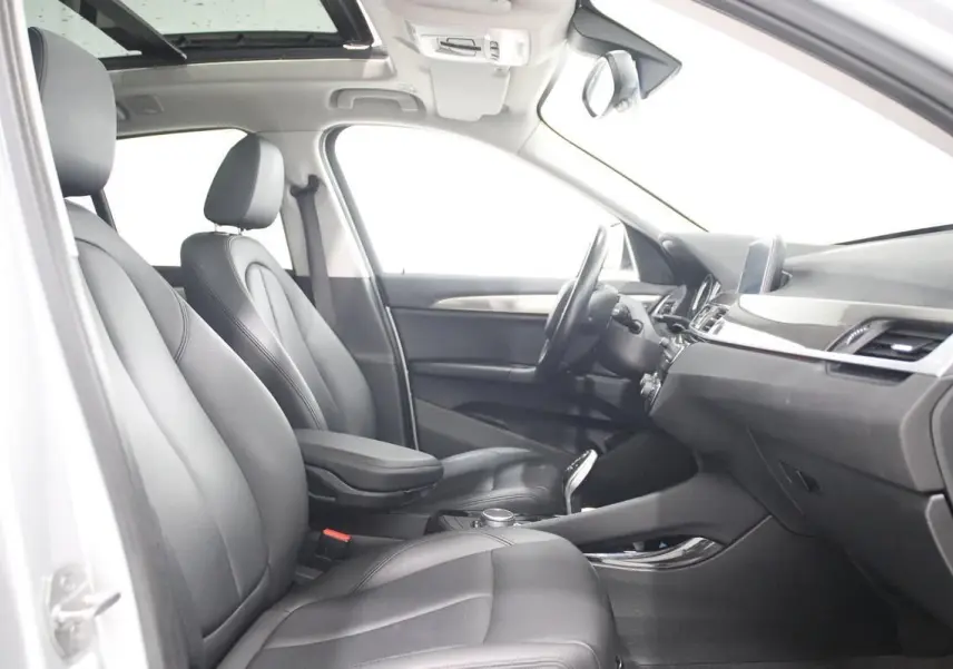 Vue intérieure côté conducteur de la BMW X1 2019, sièges cuir noirs et toit ouvrant panoramique visible.