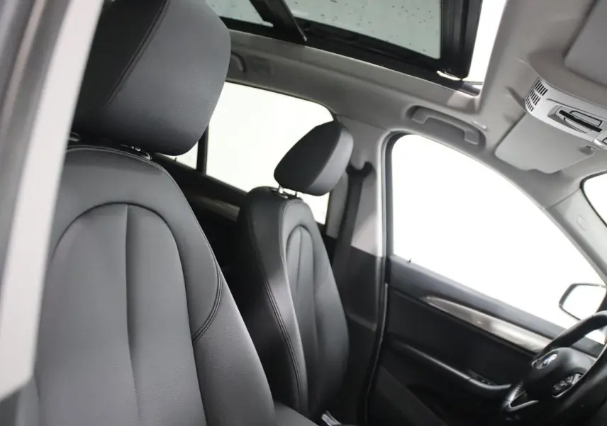 Vue intérieure côté conducteur du BMW X1 argenté 2019, montrant les sièges cuir noirs et le toit ouvrant panoramique.