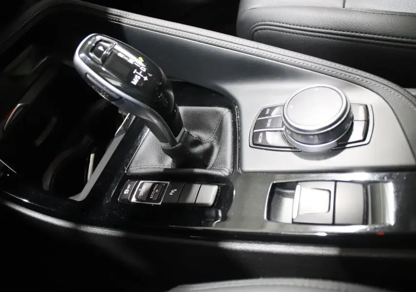 Gros plan sur la console centrale noire du BMW X1 sDRIVE 18D avec levier de vitesse automatique et commandes multimédia.