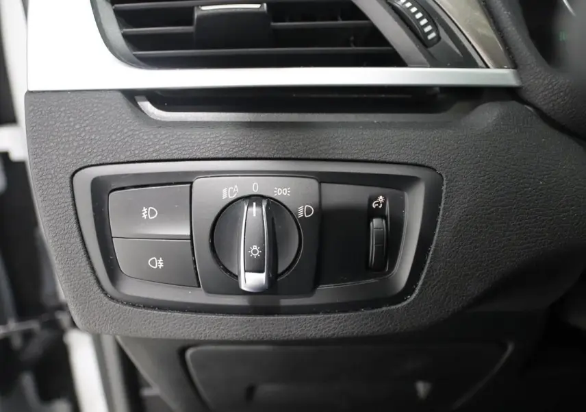 Gros plan sur le panneau de commande des phares du BMW X1 sDrive 18D, intérieur noir texturé.