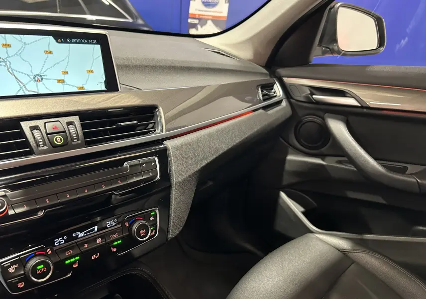 Vue intérieure côté passager du tableau de bord et console centrale d'une BMW X1 sDrive 18D argent métallisé avec écran GPS et climatisation digitale.