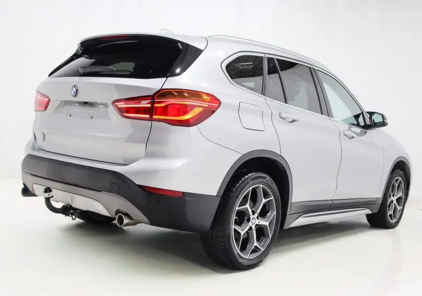 BMW X1 sDrive 18D argent métallisé vue 3/4 arrière droit avec attelage et toit ouvrant visible.