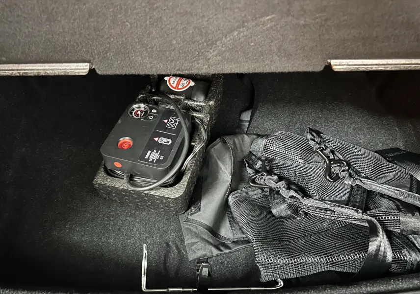 Vue intérieure du coffre d'un BMW X1 sDRIVE 18D argent métallique, montrant compresseur et filet de rangement.