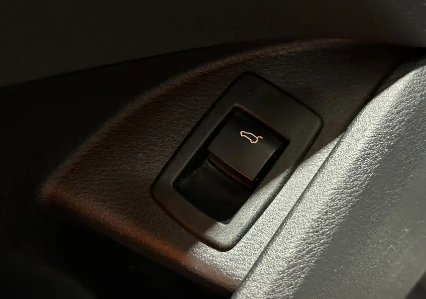 Gros plan sur le bouton d'ouverture du coffre noir, intégré dans l'habillage intérieur noir du BMW X1 sDrive 18D.
