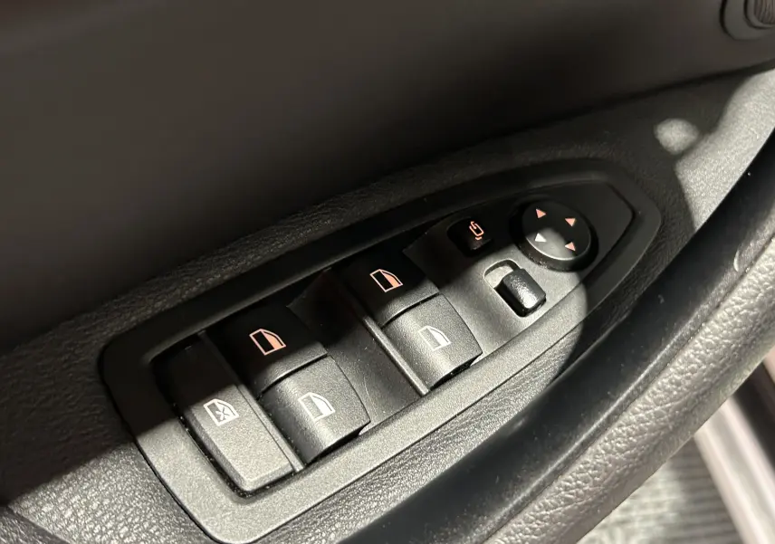 Gros plan sur les commandes de lève-vitres et réglages des rétroviseurs côté conducteur d’un BMW X1 argenté.